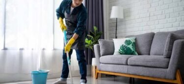 Handsome asian man wearing apron cleaning floor at home. Guy washing floor with mopping stick and bucket in living room.
